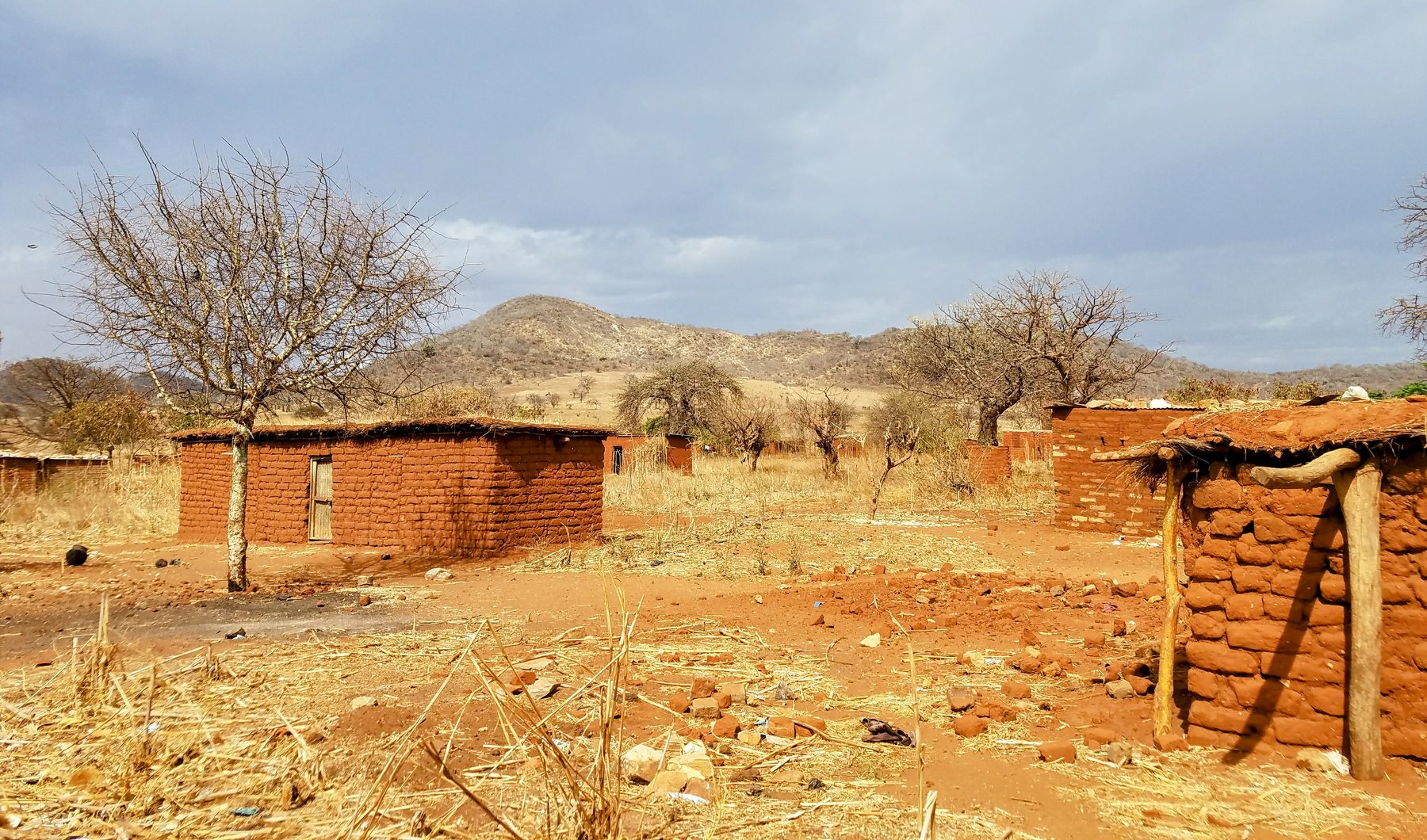 Red clay homes of Kingiti village on dry red earth, with hills behind